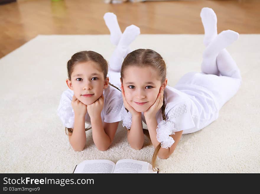 Two twin sisters at home reading a book together, studying. Two twin sisters at home reading a book together, studying