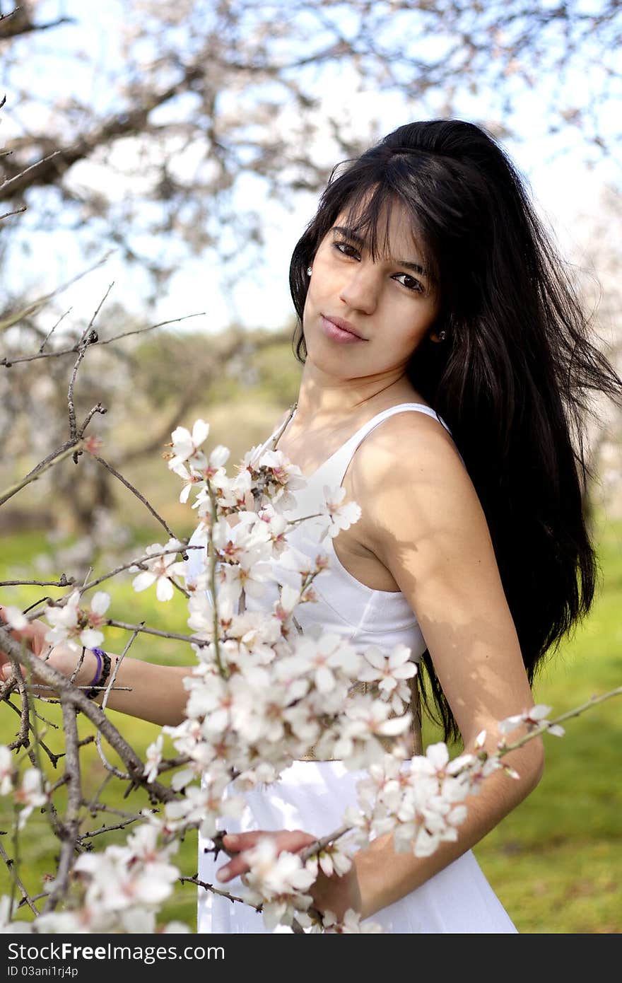 View of a beautiful girl on a white dress on a green grass field next to a almond tree. View of a beautiful girl on a white dress on a green grass field next to a almond tree