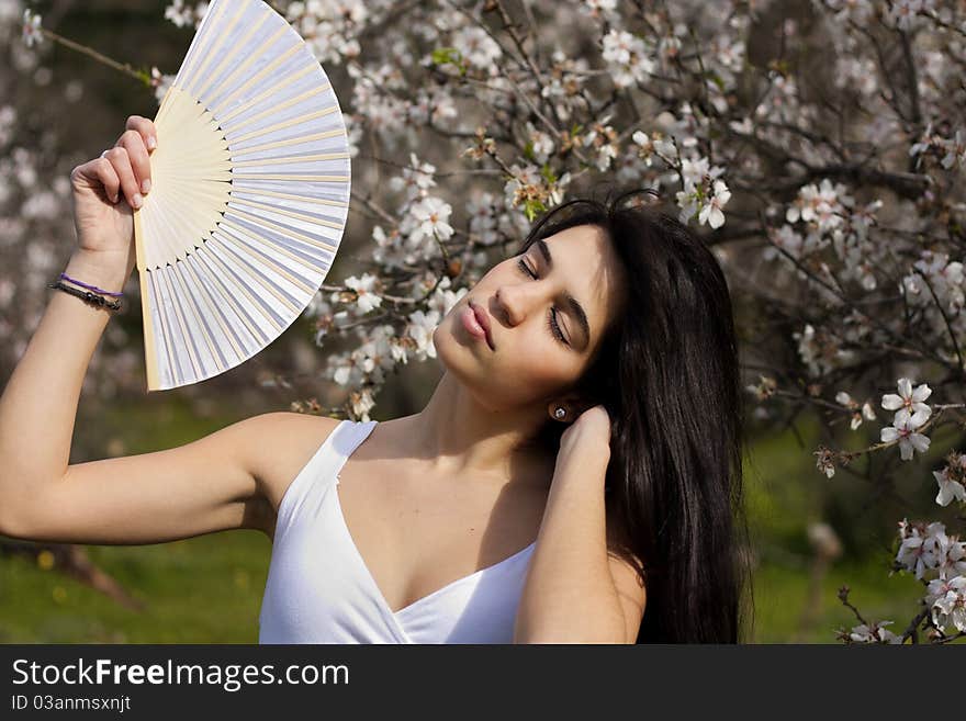 View of a beautiful girl on a white dress on a green grass field next to a almond tree. View of a beautiful girl on a white dress on a green grass field next to a almond tree