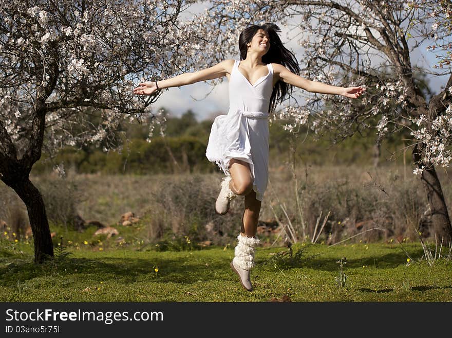 View of a beautiful girl on a white dress on a green grass field next to a almond tree. View of a beautiful girl on a white dress on a green grass field next to a almond tree