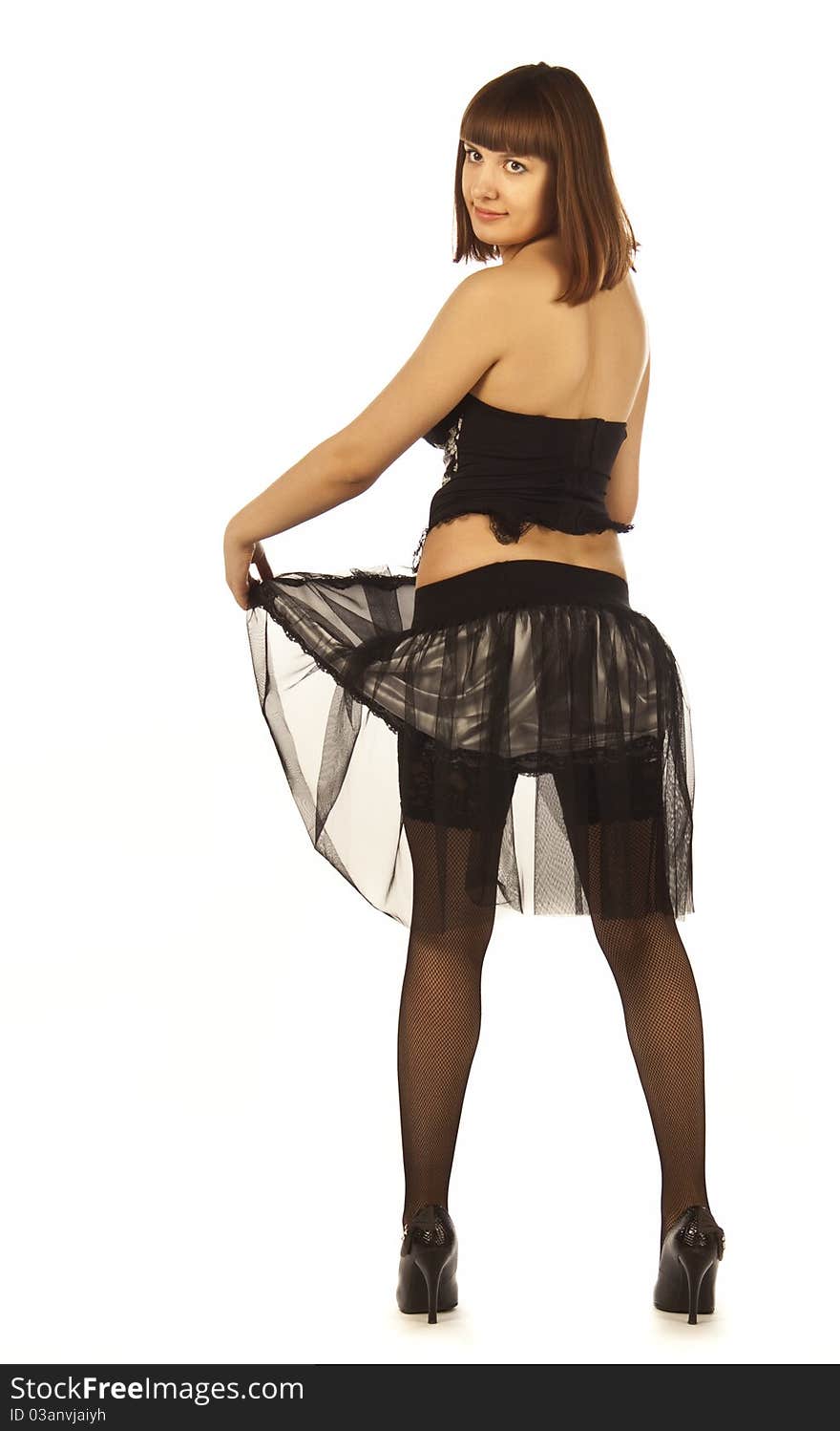 An adult woman poses in a skirt, corset, stockings, shoes on white background isolated