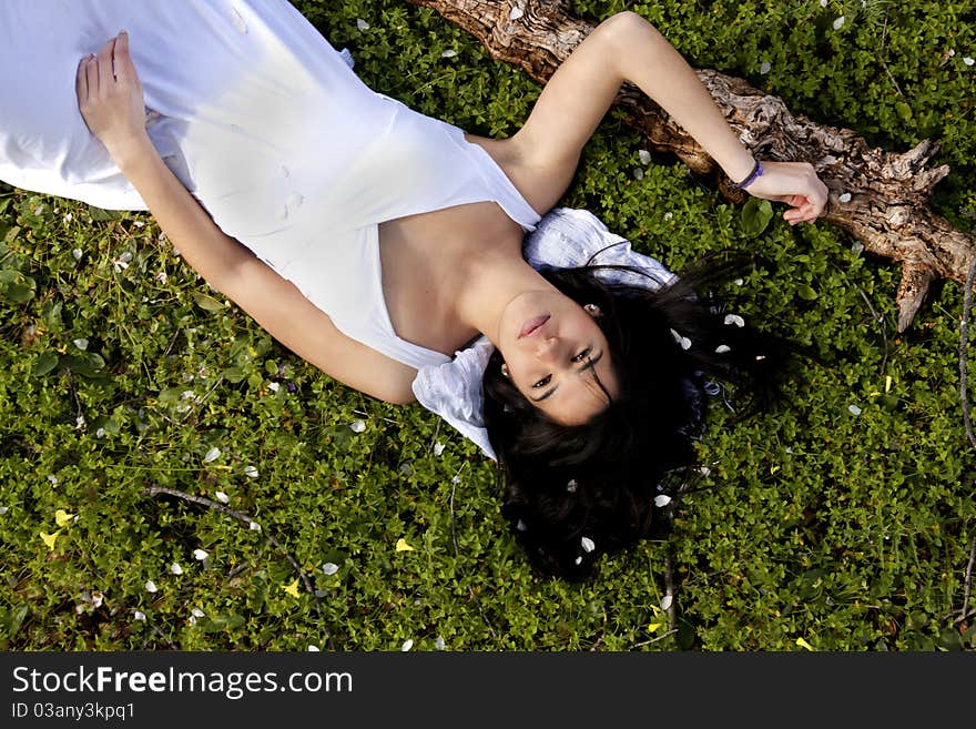 View of a beautiful girl on a white dress on a green grass field next to a almond tree. View of a beautiful girl on a white dress on a green grass field next to a almond tree