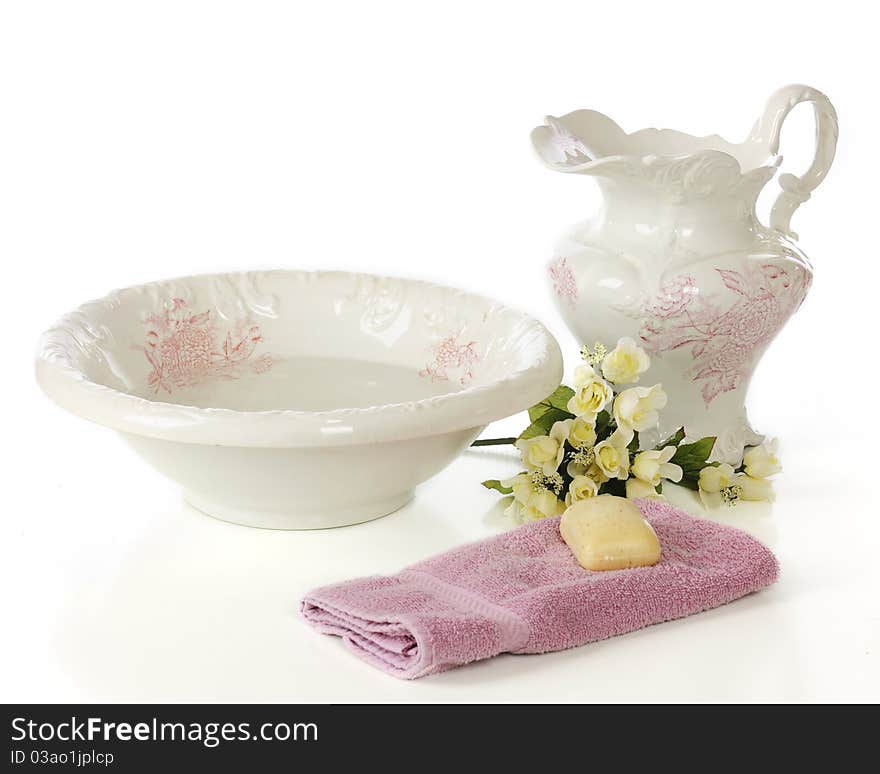 An antique bowl and pitcher with a bar of soap, hand towel and bouquet of soft yellow roses. Isolated on white. An antique bowl and pitcher with a bar of soap, hand towel and bouquet of soft yellow roses. Isolated on white.