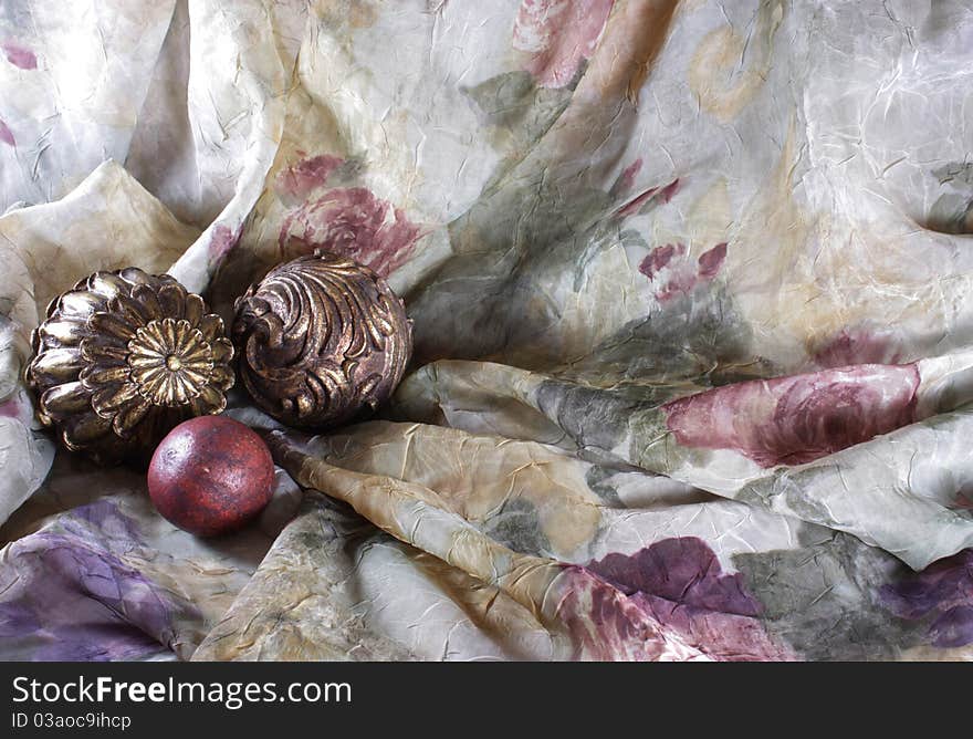 Gold balls arranged on a purple, beige, maroon and green fabric to be used as a background. Gold balls arranged on a purple, beige, maroon and green fabric to be used as a background