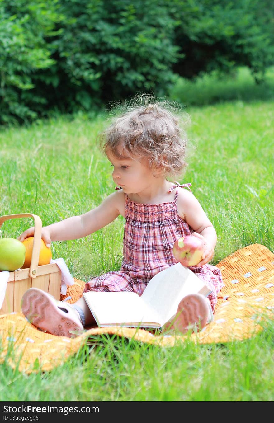 Small lovely girl with fruits and book in the park. Small lovely girl with fruits and book in the park