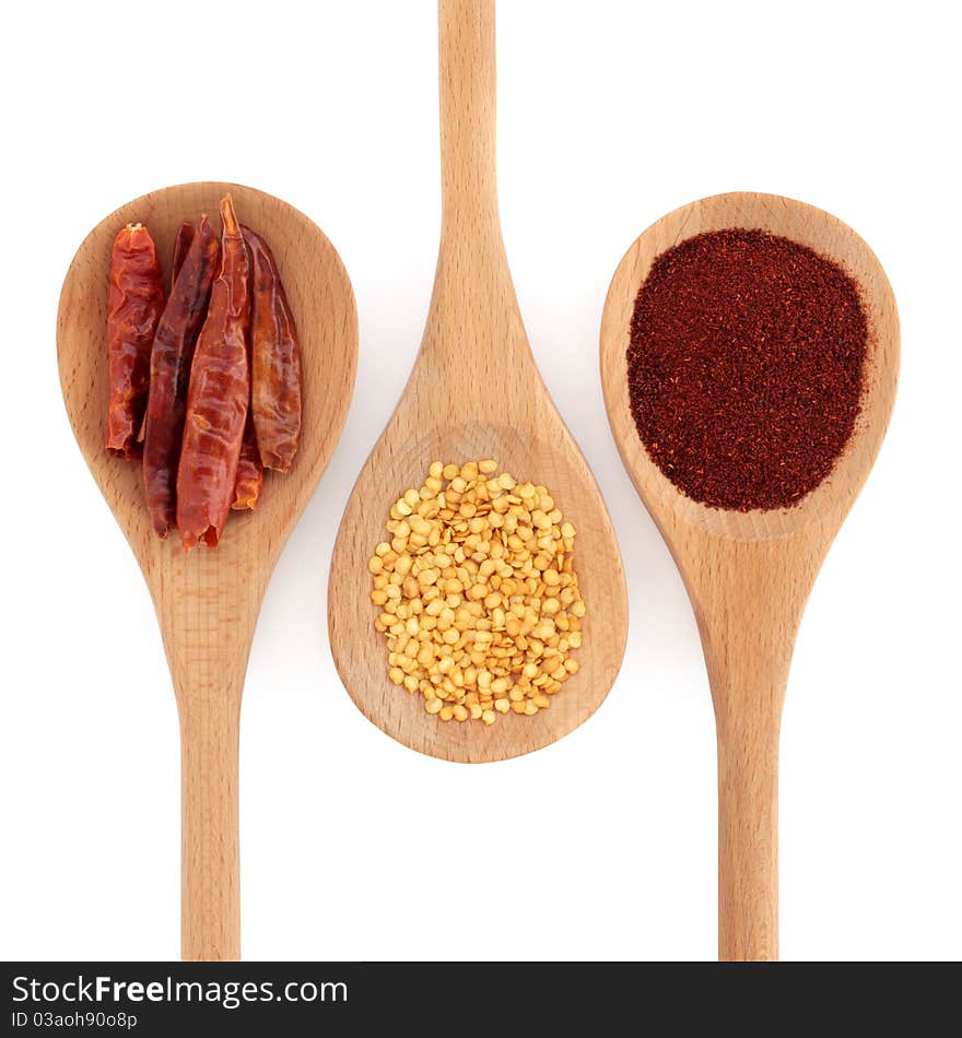 Chili spice selection of powder, seed, and dried in skin, in three wooden spoons, over white background.
