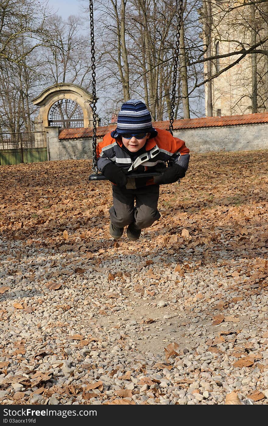 Young child with sunglasses swinging on a chain swing in a playground. Young child with sunglasses swinging on a chain swing in a playground