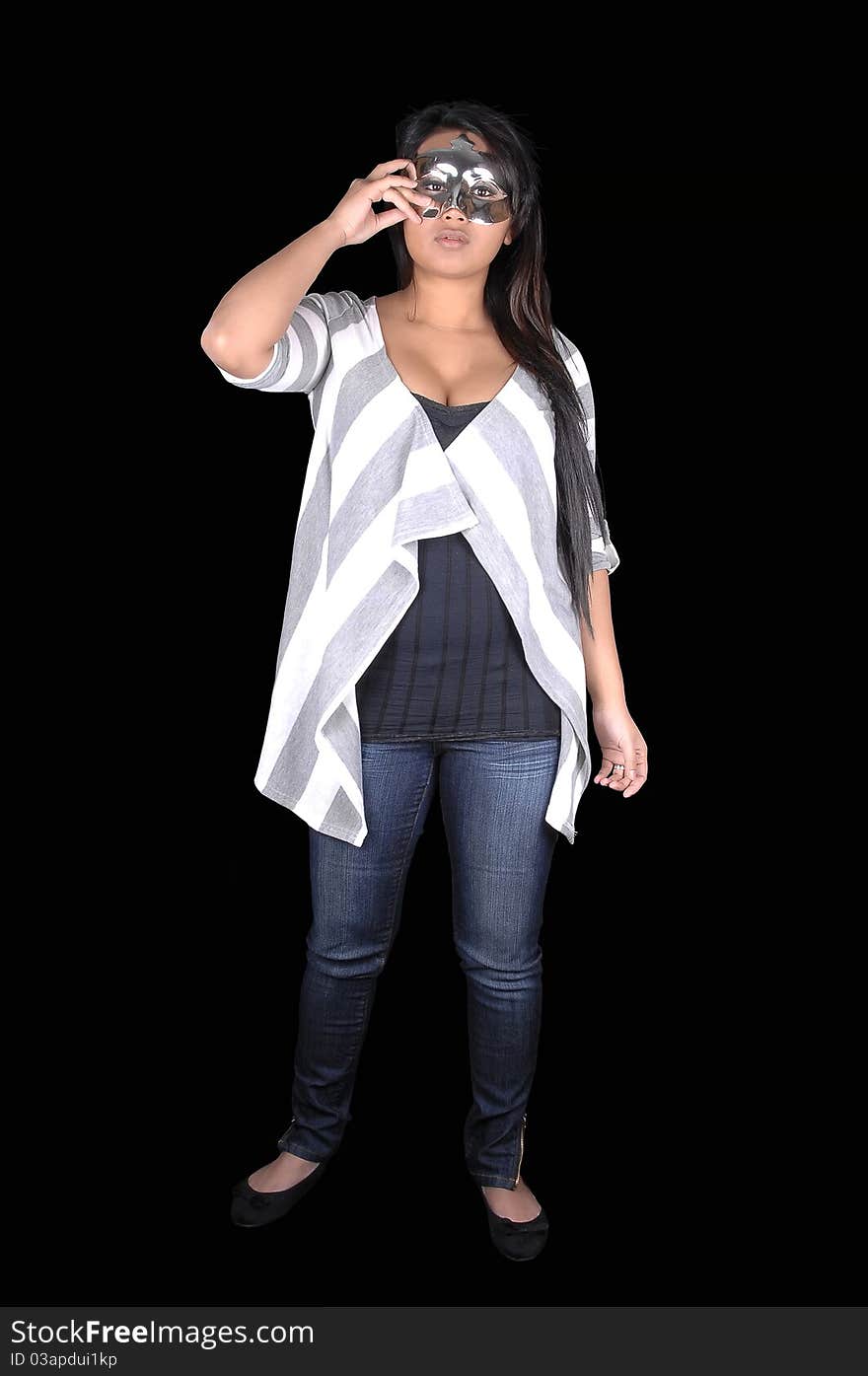 A beautiful Asian woman in jeans and a sweater standing for black background and holding a mask for her eyes. A beautiful Asian woman in jeans and a sweater standing for black background and holding a mask for her eyes.