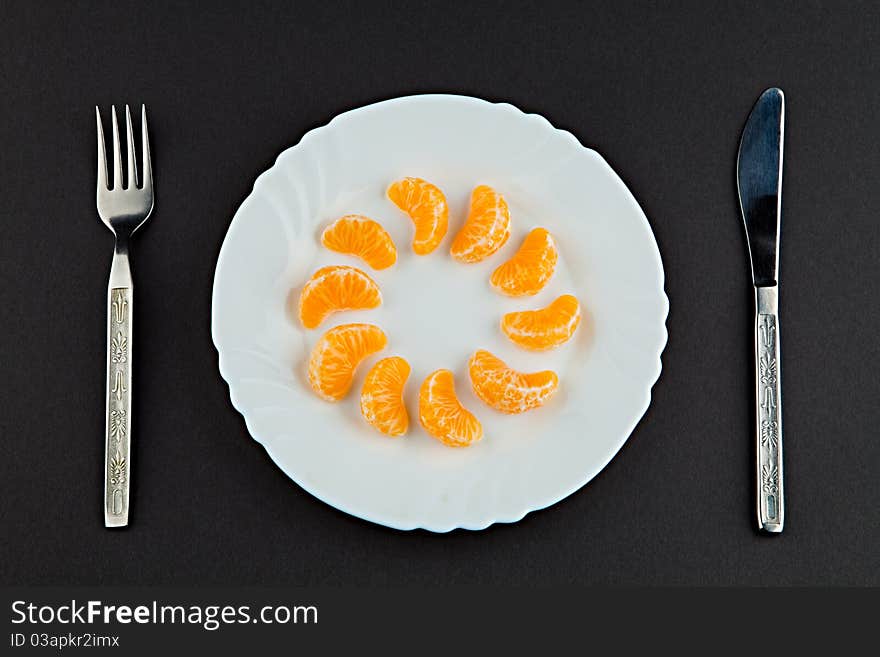 Plate with segments of a tangerine a plug and a knife against a dark background