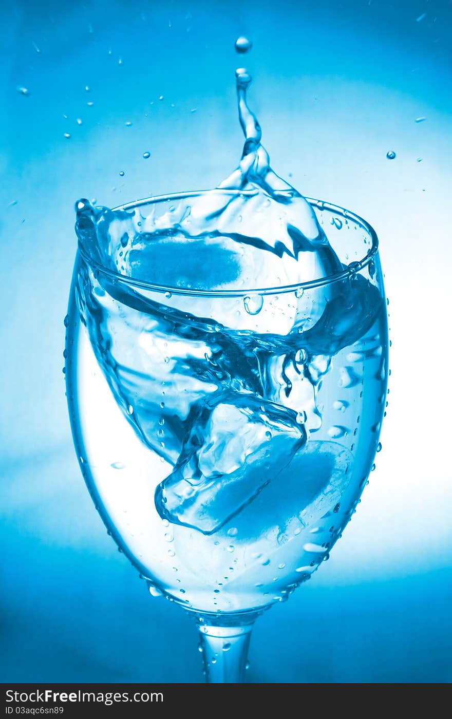 Close-up glass with water splash on blue background. Close-up glass with water splash on blue background