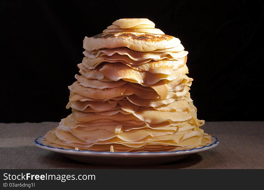 Pile of pancakes with an oil slice on a plate on black