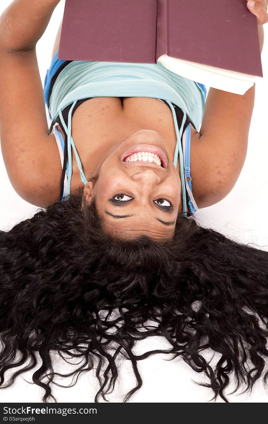 An African American woman is laying upside down with a book and a smile. An African American woman is laying upside down with a book and a smile.