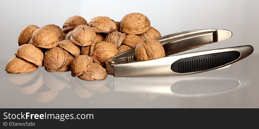 Close-up of walnut's nutshell and nutcracker on neutral background with reflection. Close-up of walnut's nutshell and nutcracker on neutral background with reflection