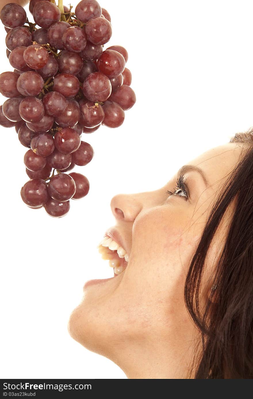 A woman is getting ready to bite into some red grapes. A woman is getting ready to bite into some red grapes.