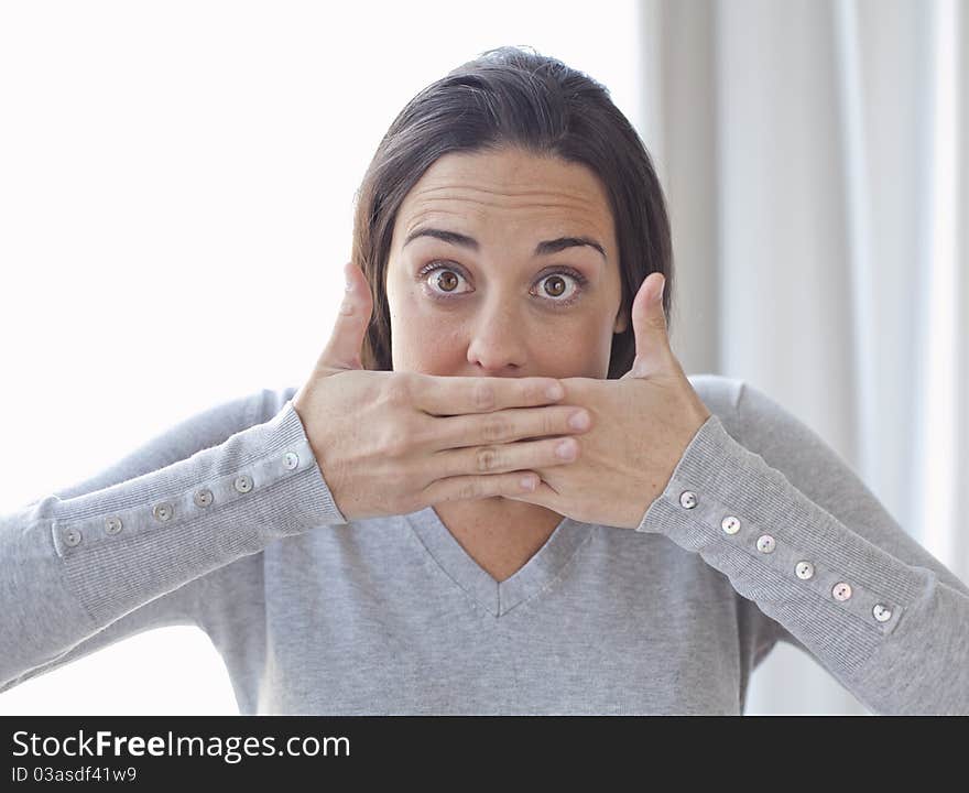 Closeup portrait of young woman covering her mouth with both hands on white