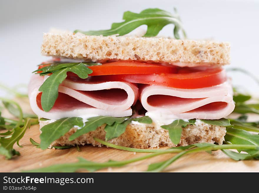 Sandwich with ham,tomato, and rucola salad on the wooden cutting board