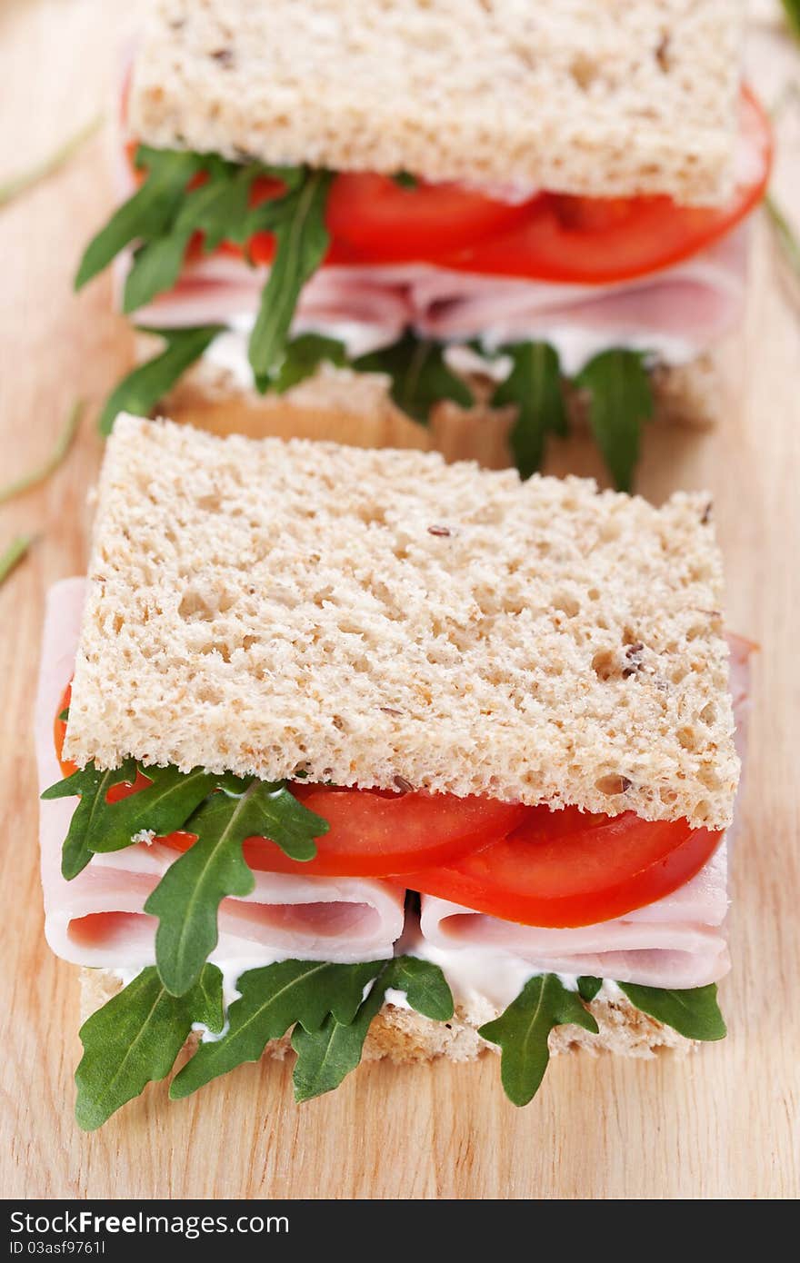 Sandwich with ham,tomato, and rucola salad on the wooden cutting board