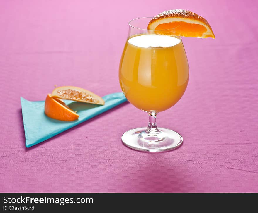 Orange juice with slices of orange on the side, presented on a pastel pink tablecloth