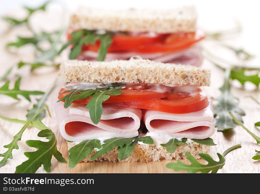 Sandwich with ham,tomato, and rucola salad on the wooden cutting board