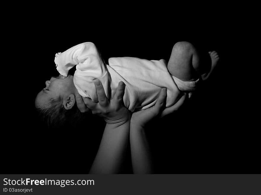 A baby being held in the air. The child is risen above. Image in black and white.