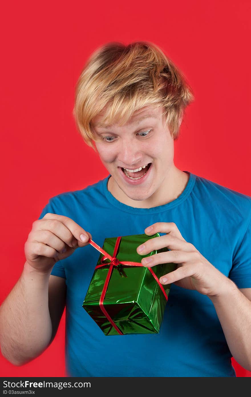 Excited young man opening a present on red background. Excited young man opening a present on red background