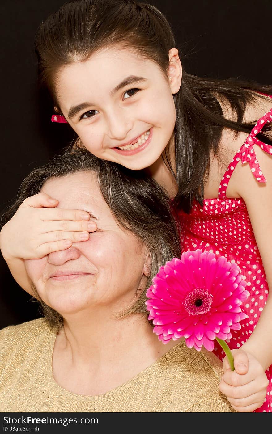 Little girl surprising her grandmother with a pink flower. Little girl surprising her grandmother with a pink flower.