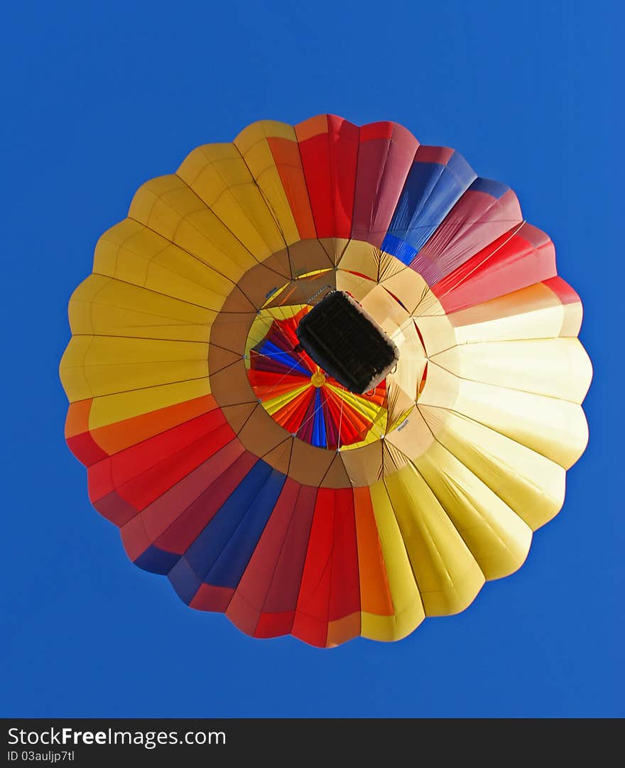 Here is a colorful hot air balloon flying directly overhead against a blue sky on a beautiful day. Here is a colorful hot air balloon flying directly overhead against a blue sky on a beautiful day.