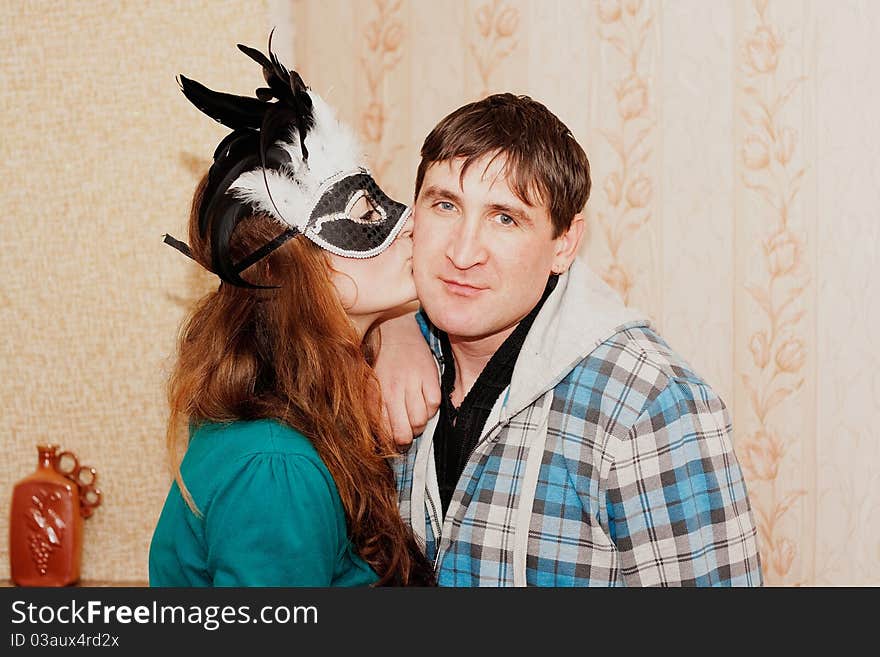 A girl kisses a guy in a mask on the cheek