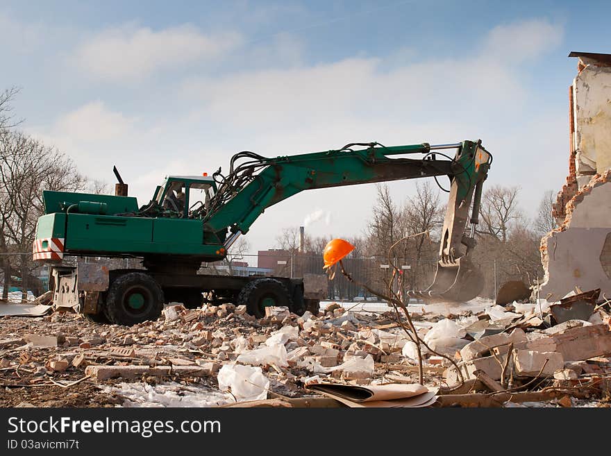 Green excavator demolished an abandoned house in construction site