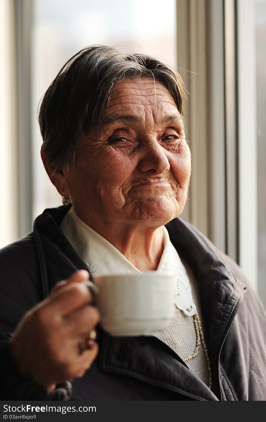 Portrait of Happy Smiling Senior Woman Beside the Window and Drinking Coffee, looking at camera. Portrait of Happy Smiling Senior Woman Beside the Window and Drinking Coffee, looking at camera