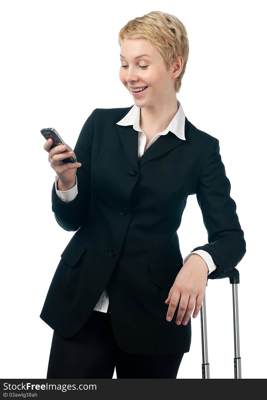 Beautiful short haired blonde business woman holding mobile phone in her hand, smiling and looking on the phone, the other hand is on suitcase handle. Isolated on white background. Beautiful short haired blonde business woman holding mobile phone in her hand, smiling and looking on the phone, the other hand is on suitcase handle. Isolated on white background