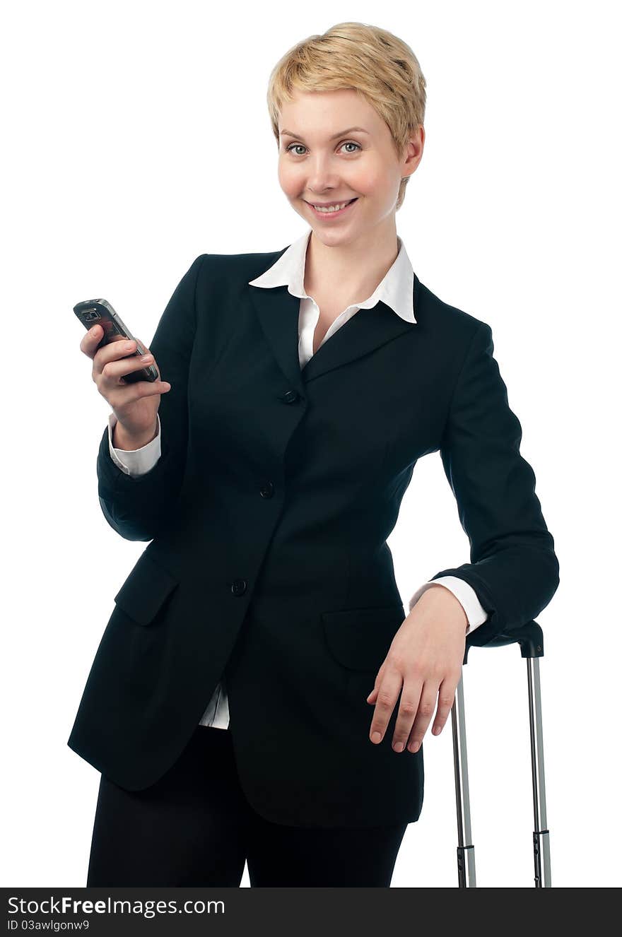 Beautiful short haired blonde business woman holding mobile phone in ger hand, smiling and looking into the camera, the other hand is on suitcase handle. Isolated on white background. Beautiful short haired blonde business woman holding mobile phone in ger hand, smiling and looking into the camera, the other hand is on suitcase handle. Isolated on white background