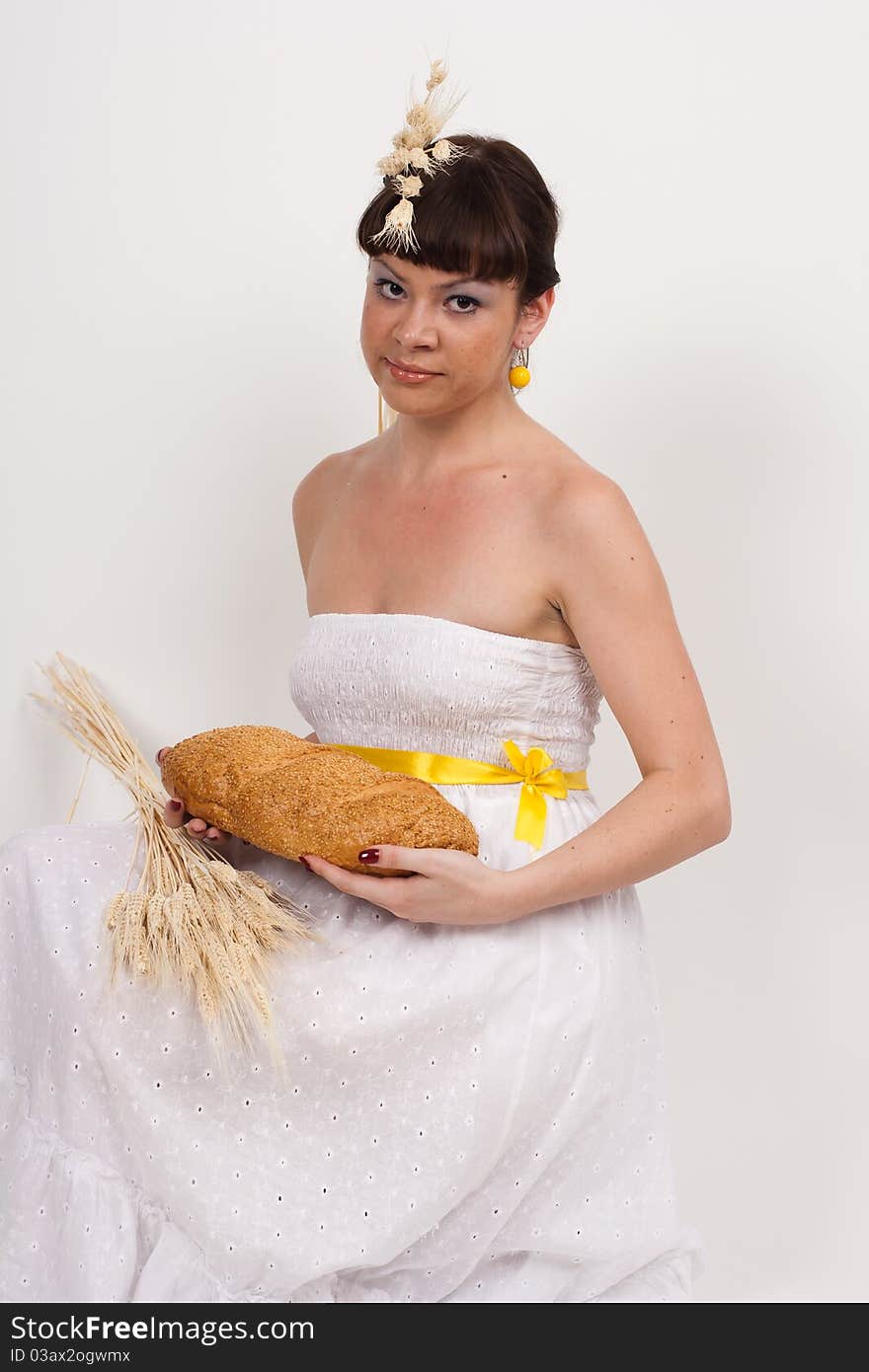 Beautiful brunette girl with ears of wheat in her hair is eating a bread isolated on the white background. Beautiful brunette girl with ears of wheat in her hair is eating a bread isolated on the white background