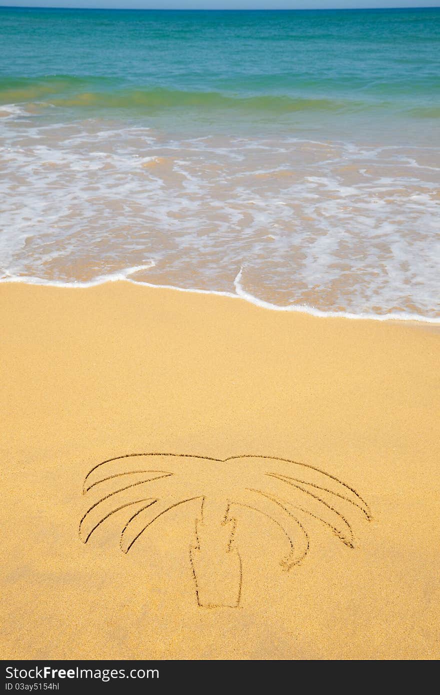 A palm tree written on the sand of a beach with a wave approaching