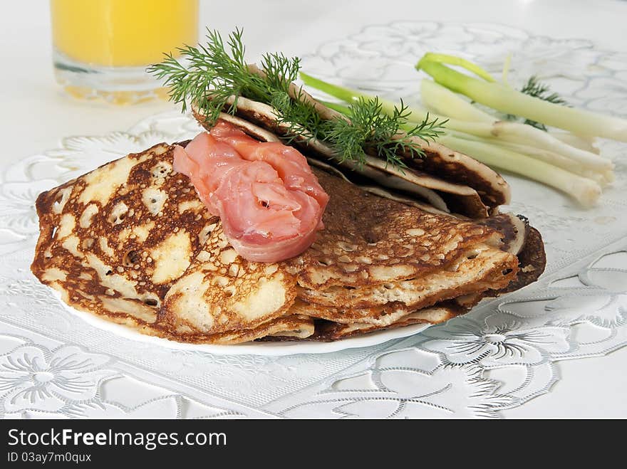 On a table there is a plate with pancakes and red fish. On a light background. On a table there is a plate with pancakes and red fish. On a light background