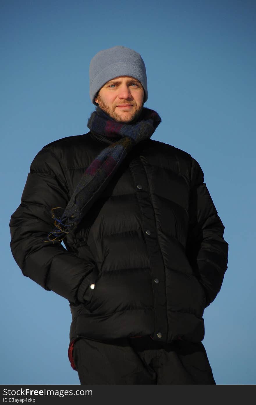 Attractive man with beard poses in warm jacket on cold winter's day, against bright blue sky. Attractive man with beard poses in warm jacket on cold winter's day, against bright blue sky