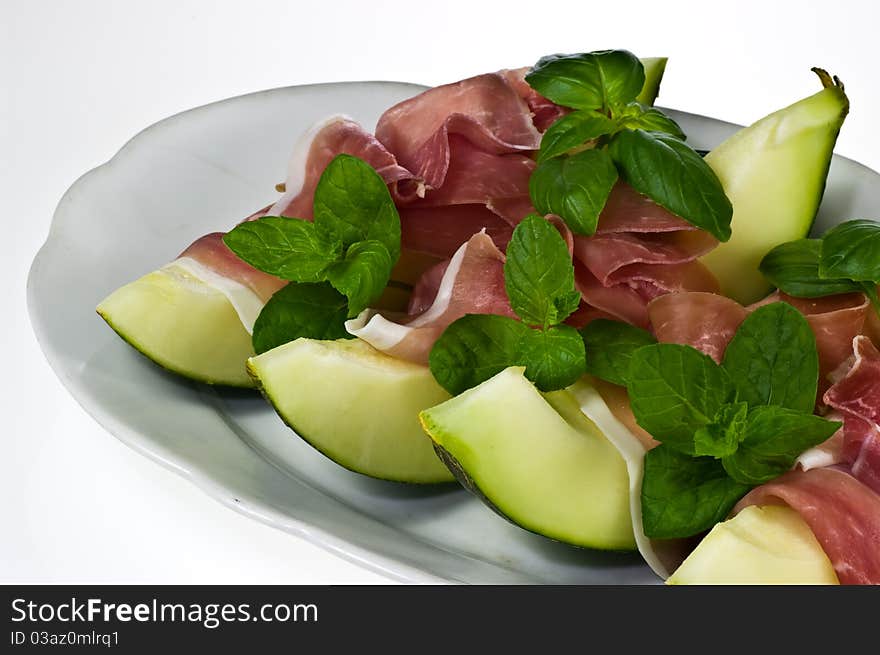 Melon with italian ham and basil leaves on porcelain dish. Melon with italian ham and basil leaves on porcelain dish