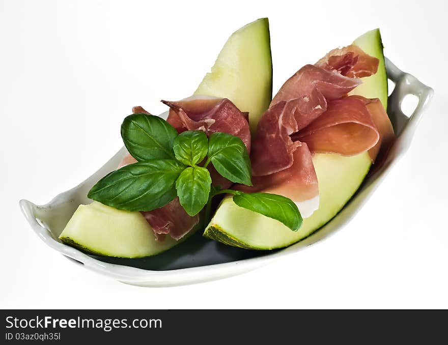 Melon with italian ham and basil leaves on porcelain dish. Melon with italian ham and basil leaves on porcelain dish