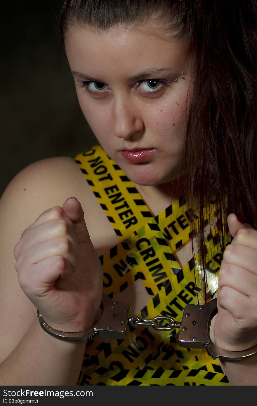 Portrait of young woman with police crime scene tape on body and handcuffs; black background. Portrait of young woman with police crime scene tape on body and handcuffs; black background.