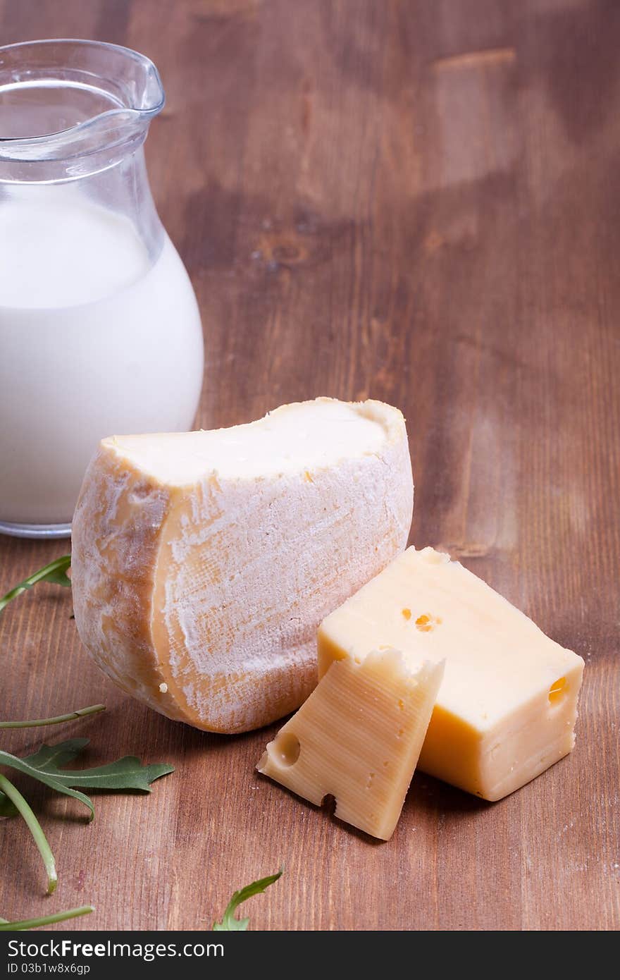 Composition with tow kind of cheese and jug of milk on the wooden table. Composition with tow kind of cheese and jug of milk on the wooden table