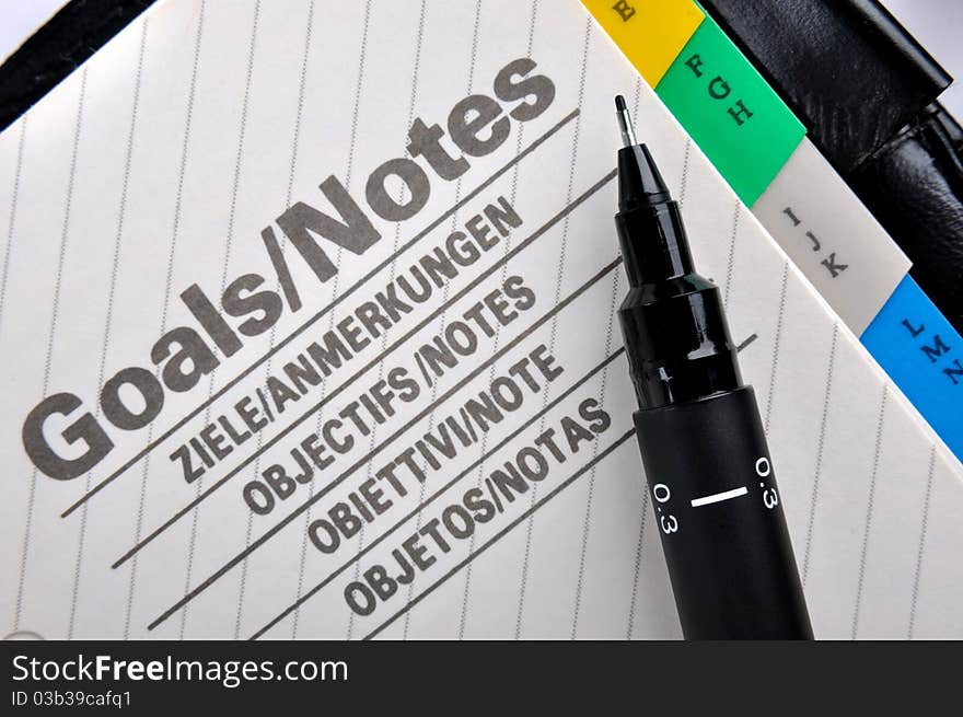 Goals plan or record in notepad and a pen, shown as working goals, target, focus, objective important notes and other related business concept. Goals plan or record in notepad and a pen, shown as working goals, target, focus, objective important notes and other related business concept.