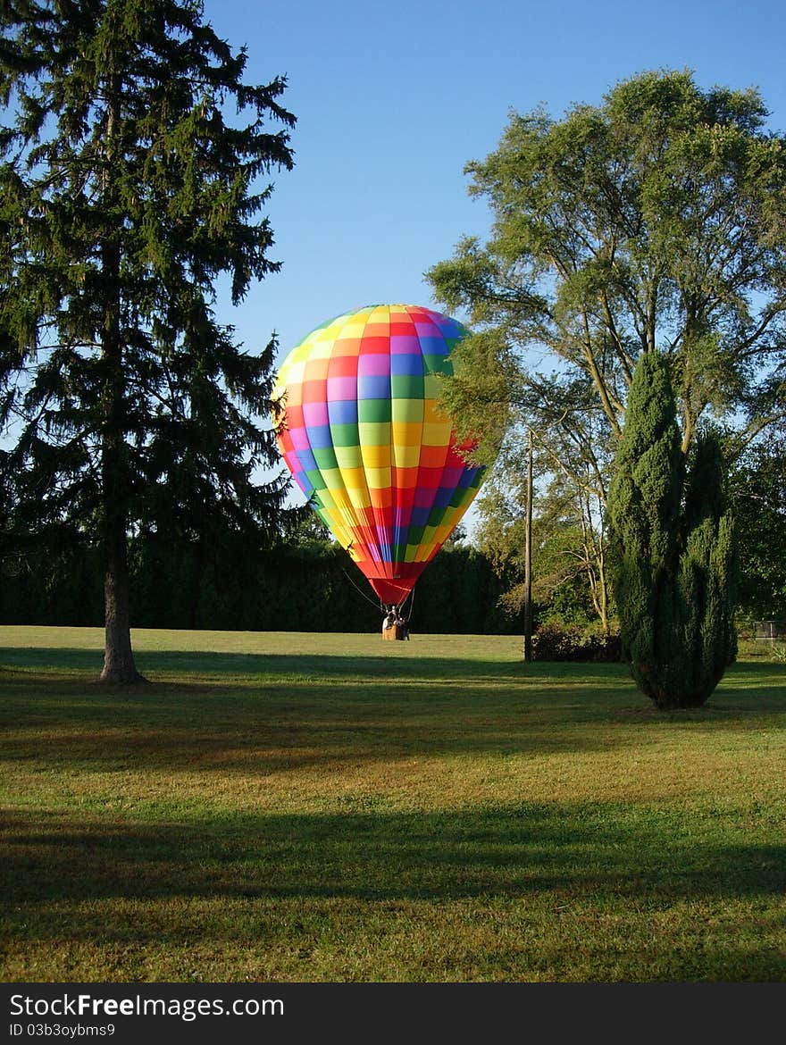 A Hot Air Balloon Landing In A Beautiful Grassy Field Surrounded By Trees. A Hot Air Balloon Landing In A Beautiful Grassy Field Surrounded By Trees