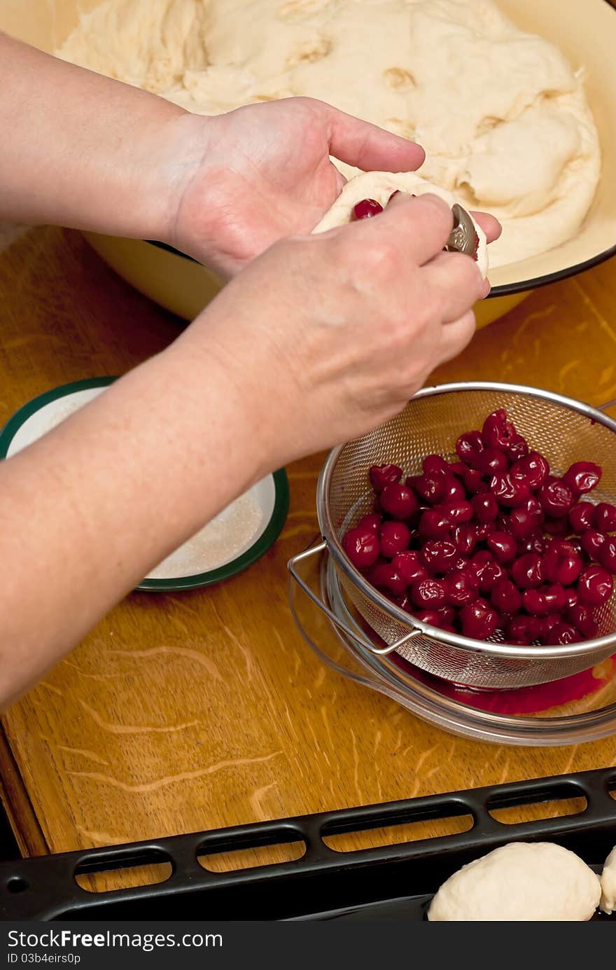 Female hands making small pies with cherry on a table. Female hands making small pies with cherry on a table