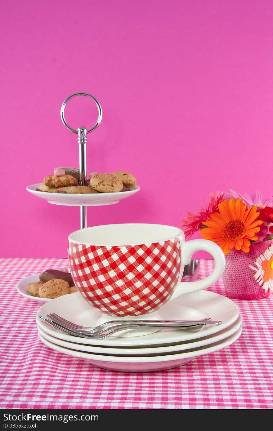 A cup and saucer on a checkered tablecloth and a serving bowl with cookies and chocolate. A cup and saucer on a checkered tablecloth and a serving bowl with cookies and chocolate