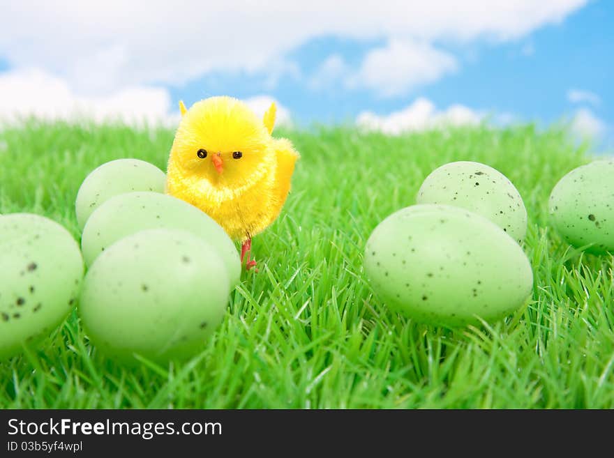 A yellow chick with easter eggs on a green lawn against a cloudy sky