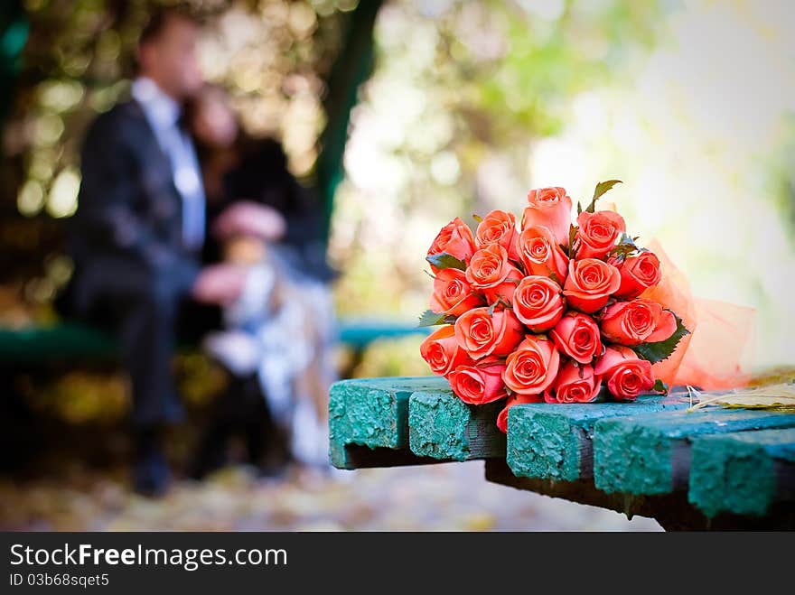 Bridal bouquet of red roses on a green meadow and blurred newlyweds. Bridal bouquet of red roses on a green meadow and blurred newlyweds