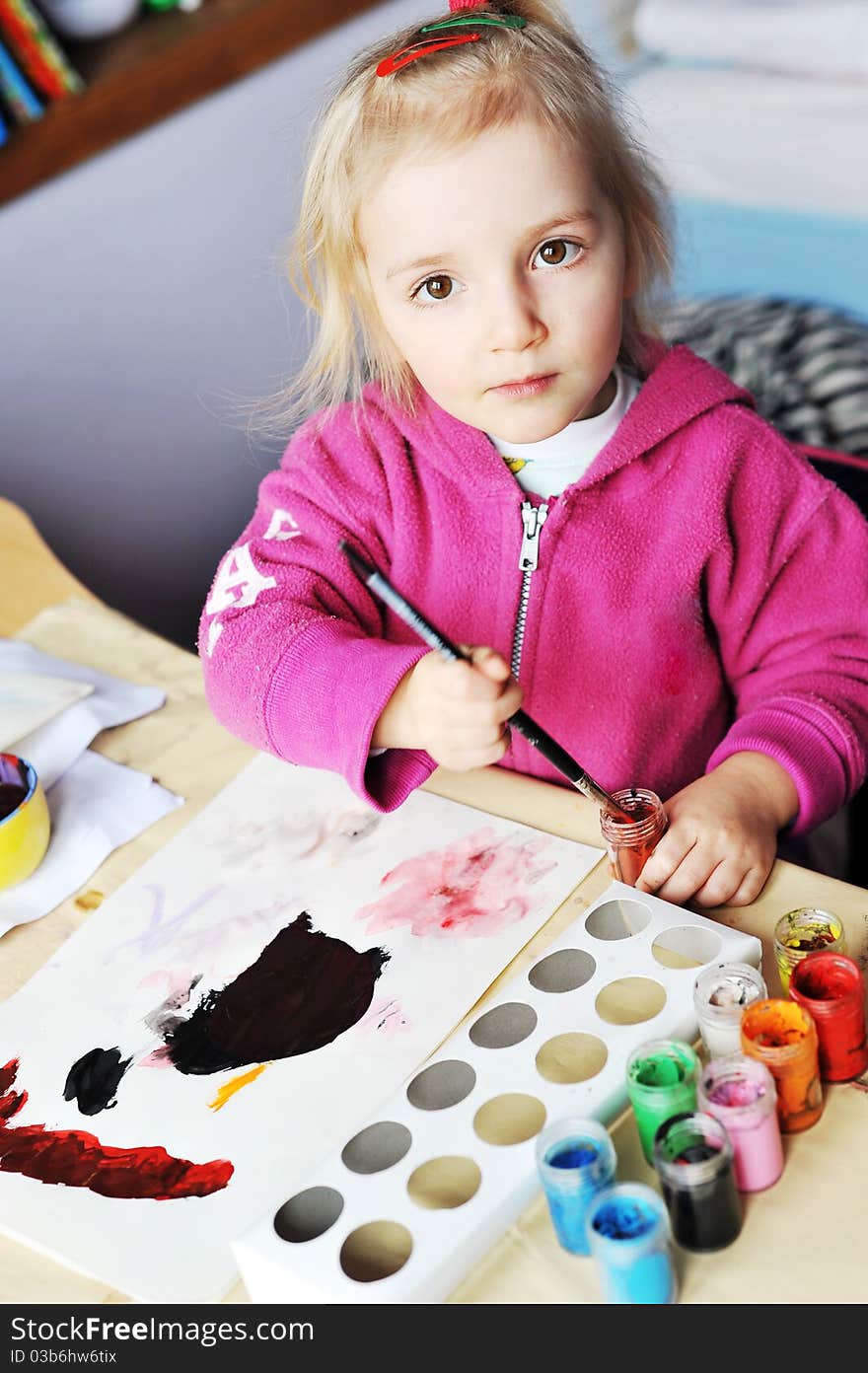 Beautiful little girl is drawing with gouaches on paper