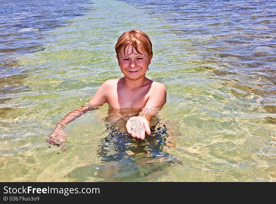 Boy has fun in the clear atlantic ocean and holds a shell with sand in the hand. Boy has fun in the clear atlantic ocean and holds a shell with sand in the hand