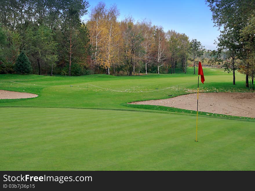 Golf meadow and autumnal forest. Red flag.