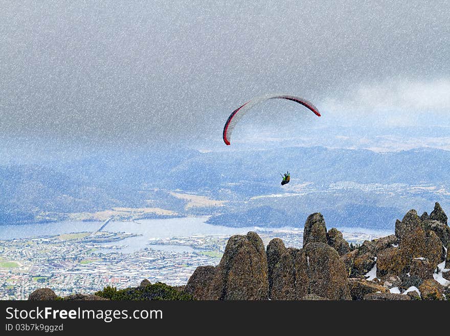 A paraglider hovers over Mount Wellington in Tasmania while it snows. A paraglider hovers over Mount Wellington in Tasmania while it snows.